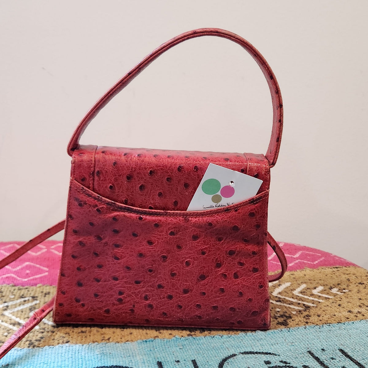 Back view of vintage Mike's Collection red ostrich-embossed leather mini handbag with Lucille Golden Vintage tag in the slip pocket