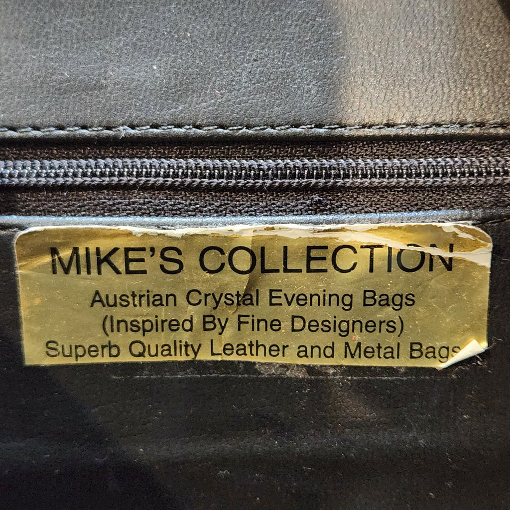 Detailed close-up of the gold Mike's Collection designer label inside the vintage red ostrich-embossed leather mini handbag, reading Austrian Crystal Evening Bags, Inspired By Fine Designers, Superb Quality Leather and Metal Bags