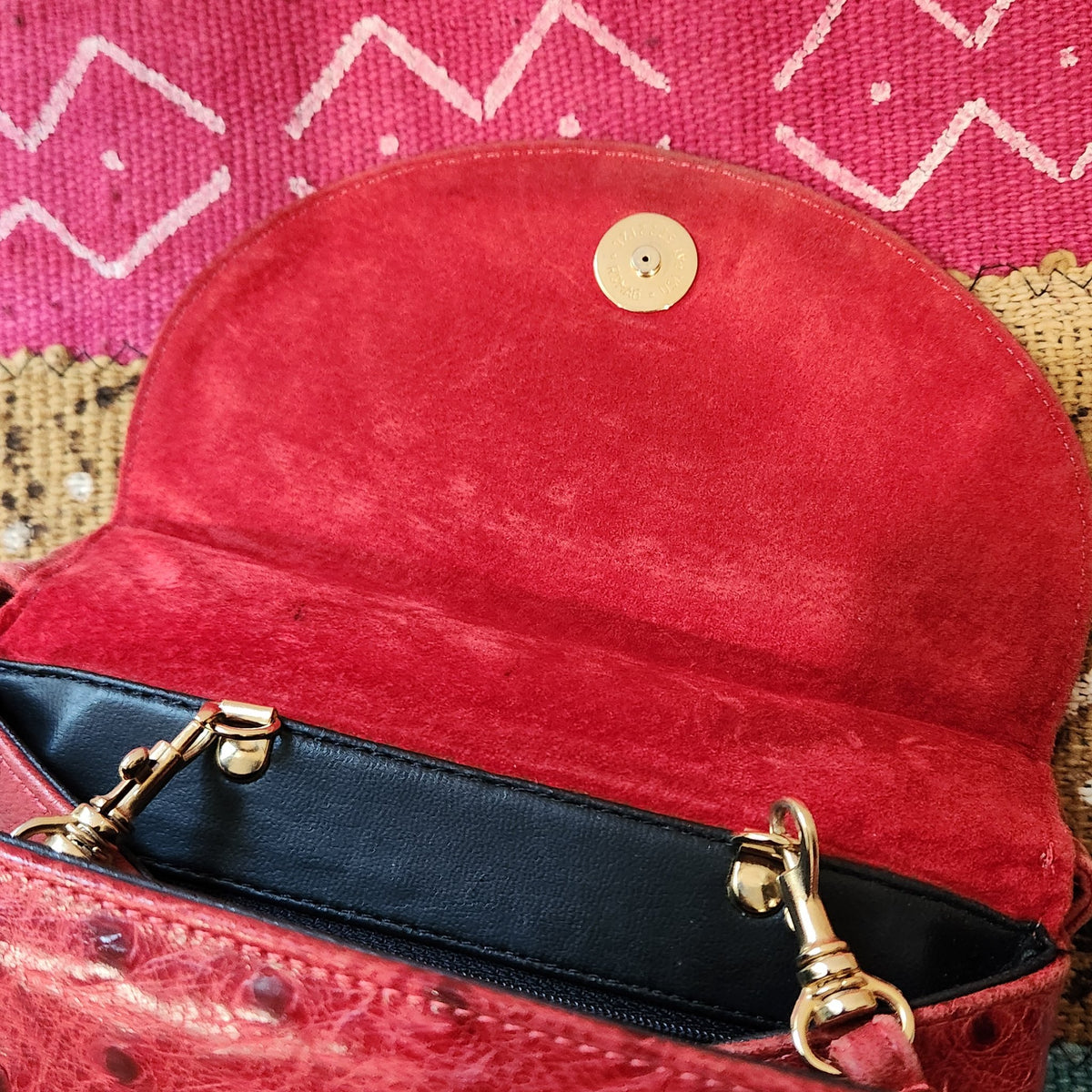 Underside of the rounded flap of vintage Mike's Collection red ostrich-embossed leather mini handbag, showing red suede lining and gold-tone magnetic snap