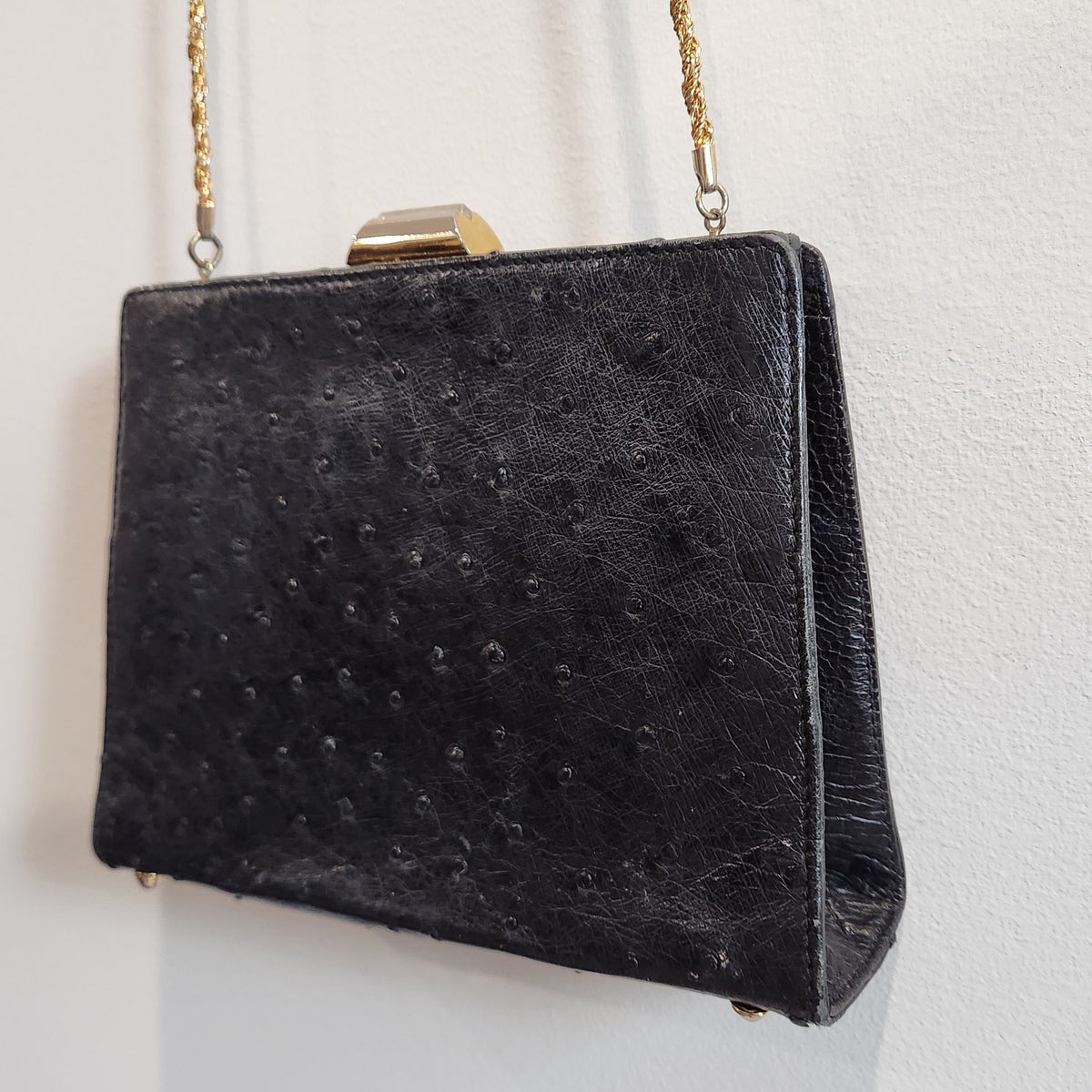 Close-up angled front view of vintage Beoni Lucia black ostrich-textured leather evening bag, showing raised follicle texture and gold-tone clasp