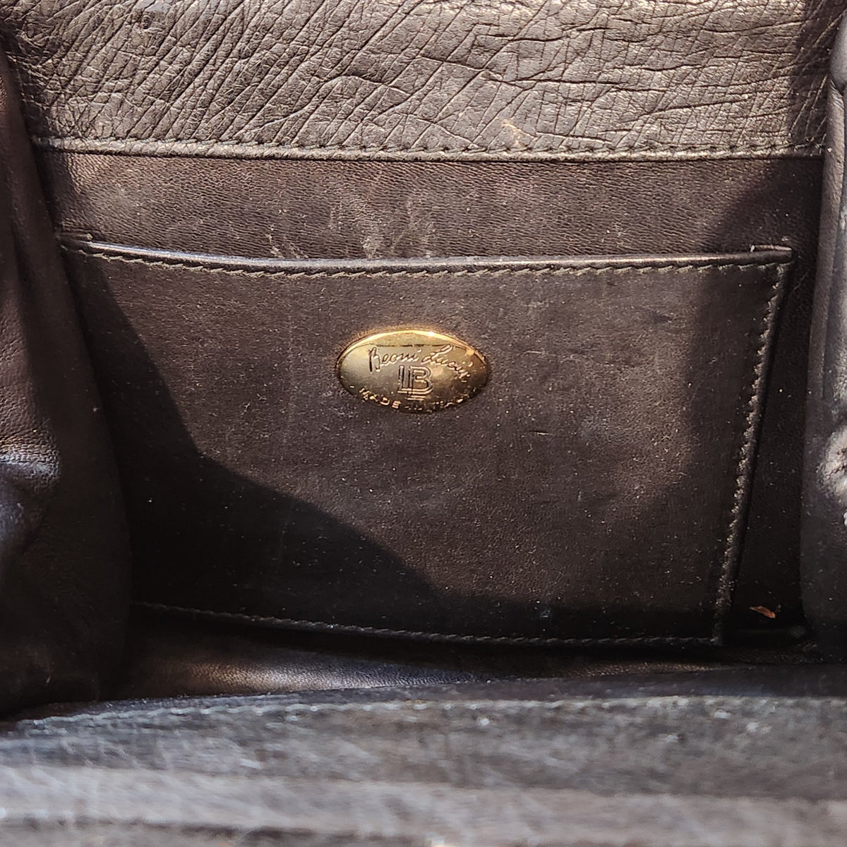 Interior slip pocket of vintage Beoni Lucia black evening bag with gold oval Beoni Lucia designer plaque, showing lining wear