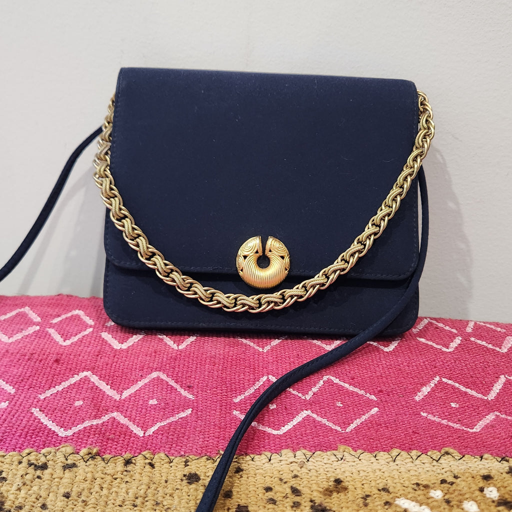 Original photo: vintage Kenneth Jay Lane midnight navy flap bag with gold chain draped across the front, on a pink textile