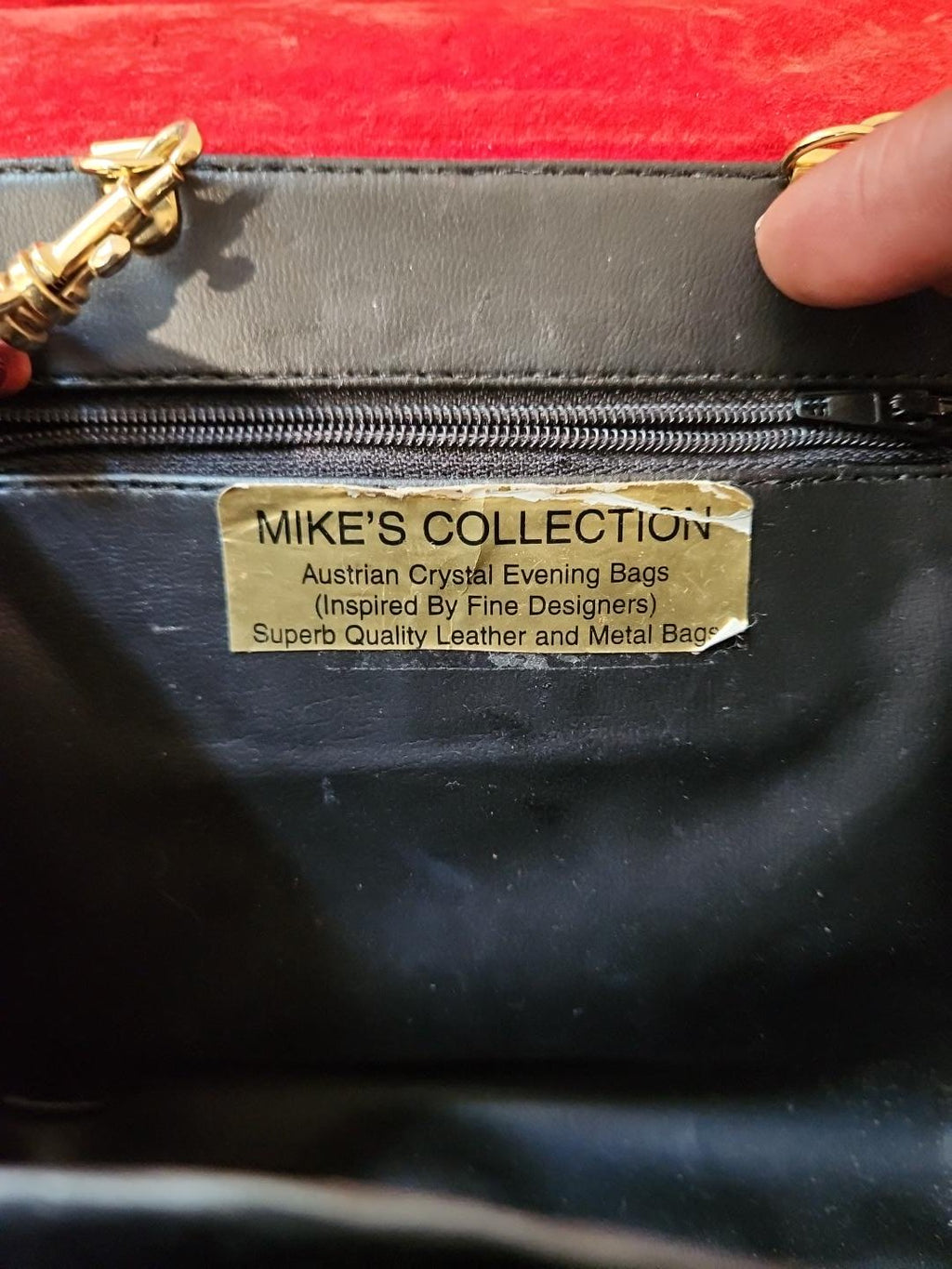 Close-up of the gold Mike's Collection designer label inside the vintage red ostrich-embossed leather mini handbag, showing age-related wear and peeling at the edges