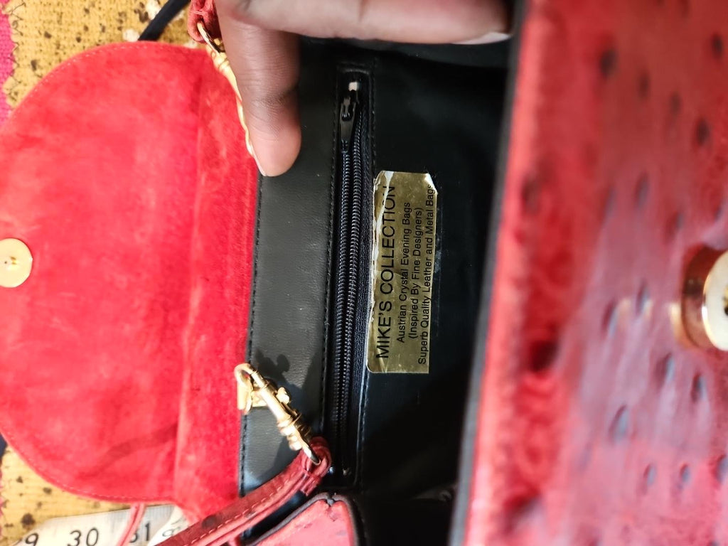 Interior of vintage Mike's Collection red ostrich-embossed leather mini handbag, open to show red suede flap underside, black vinyl lining, interior zippered compartment and designer label