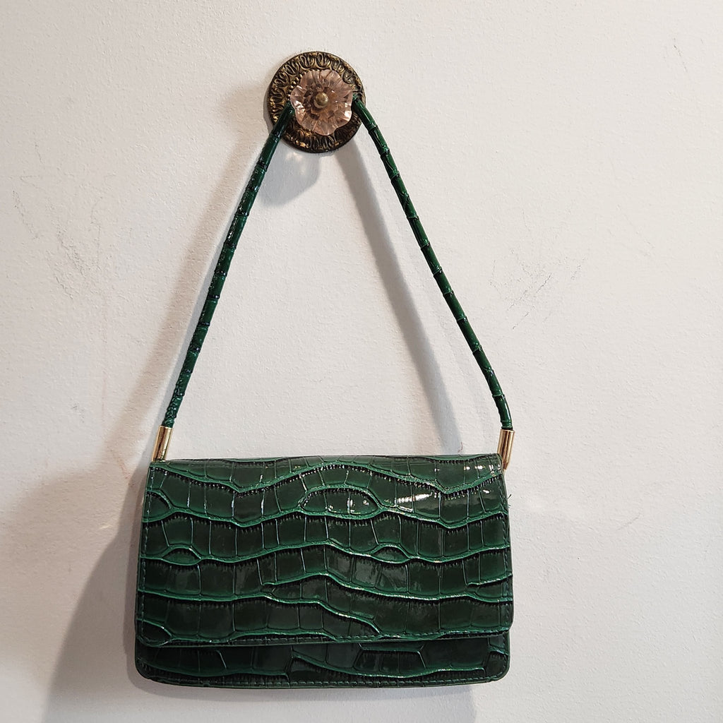 Forest green croc-embossed shoulder bag hanging from a wall hook, front view
