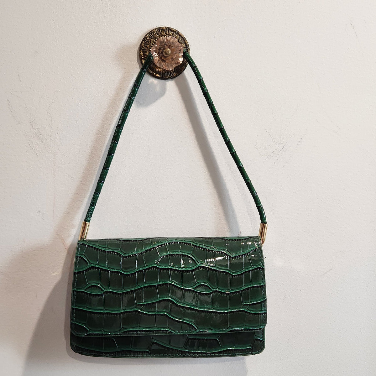 Forest green croc-embossed shoulder bag hanging from a wall hook, front view
