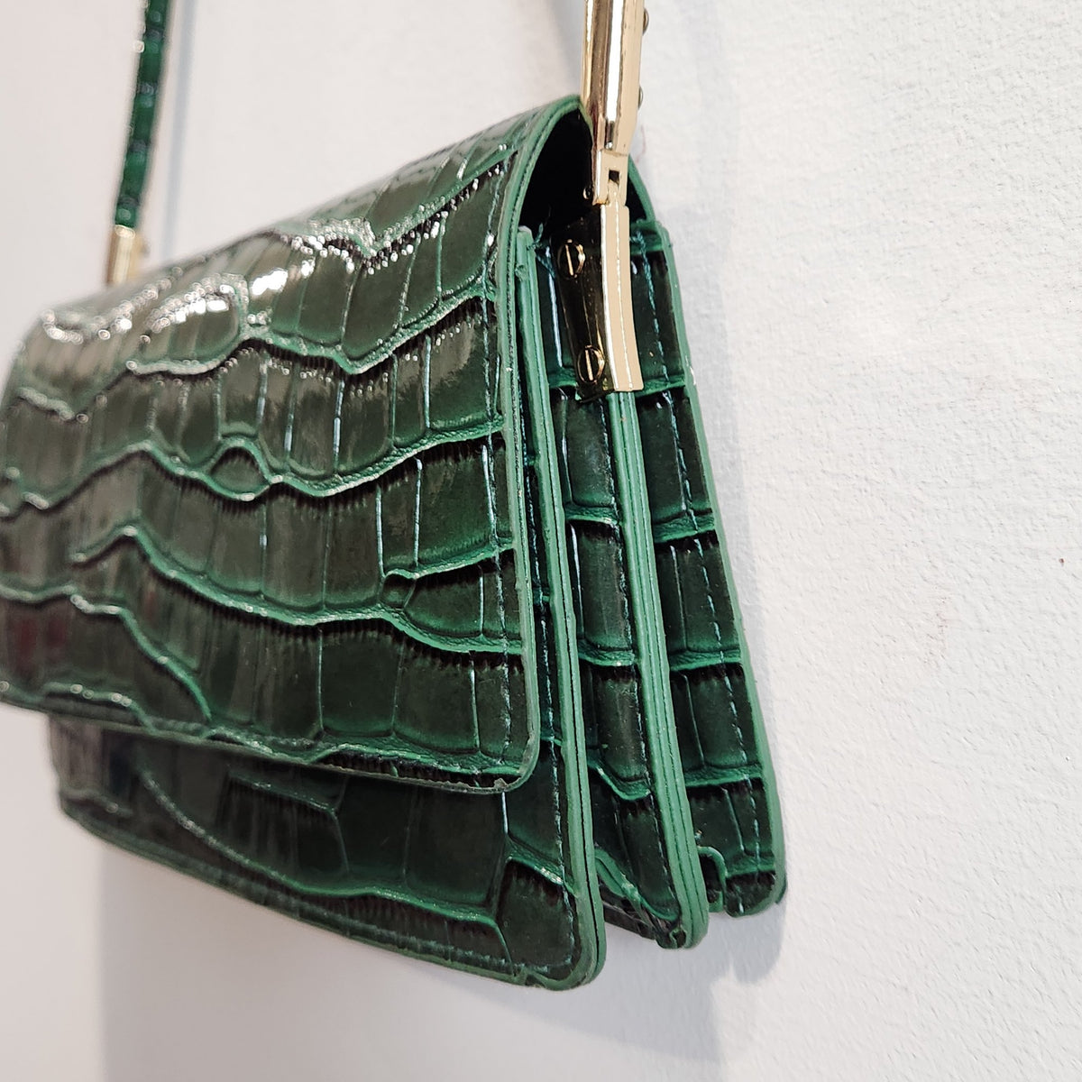 Side and gusset close-up of the forest green croc-embossed shoulder bag with gold-tone strap hardware