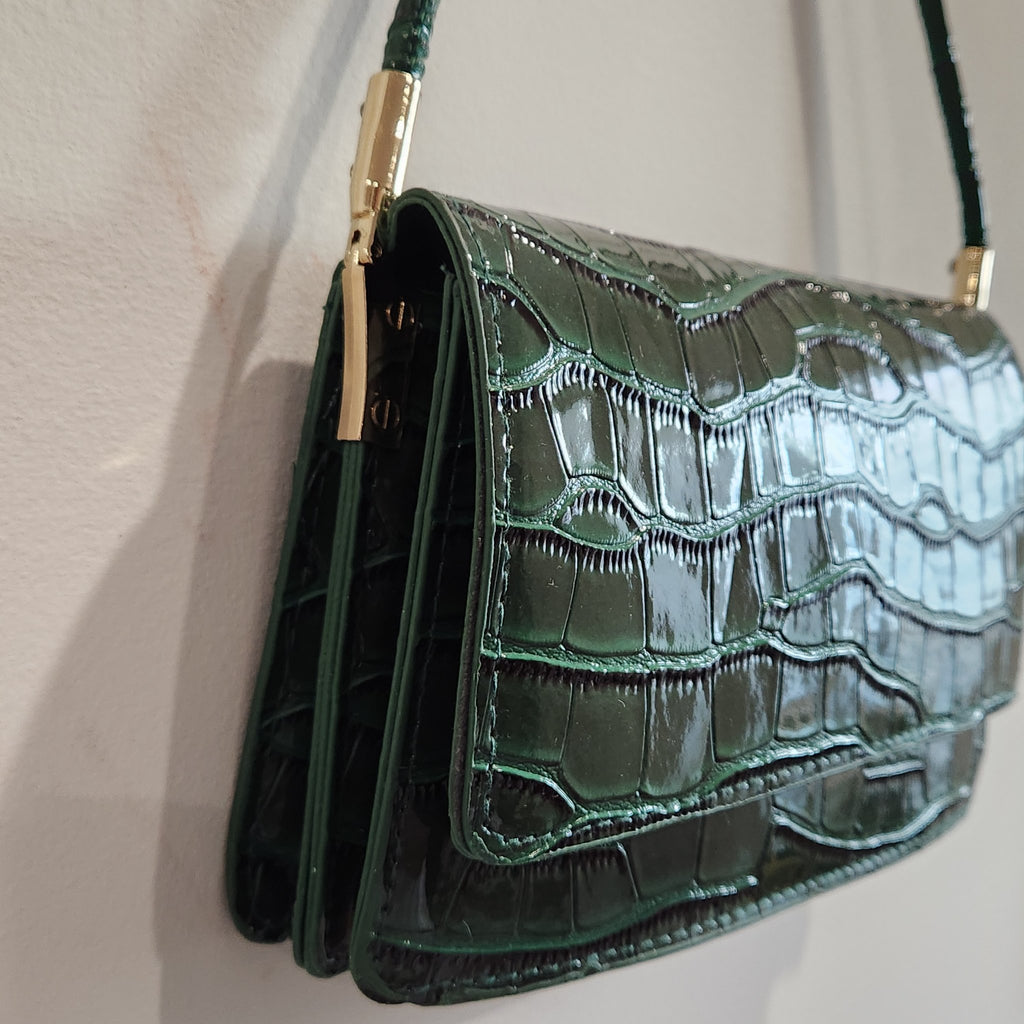 Angled side view of the forest green croc-embossed shoulder bag showing the gusseted construction and gold-tone hardware