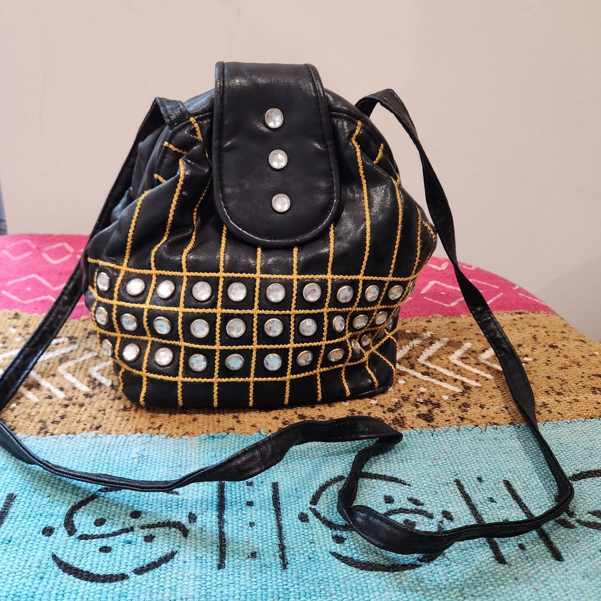 Original photo: black embellished bucket shoulder bag, front view on a patterned textile, long shoulder strap