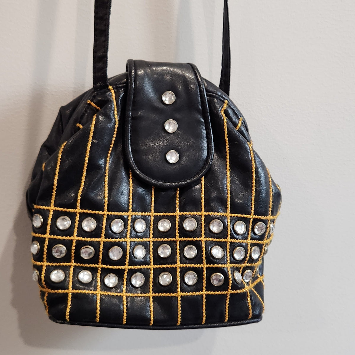 Original photo: black embellished bucket shoulder bag hanging by its long shoulder strap against a white wall