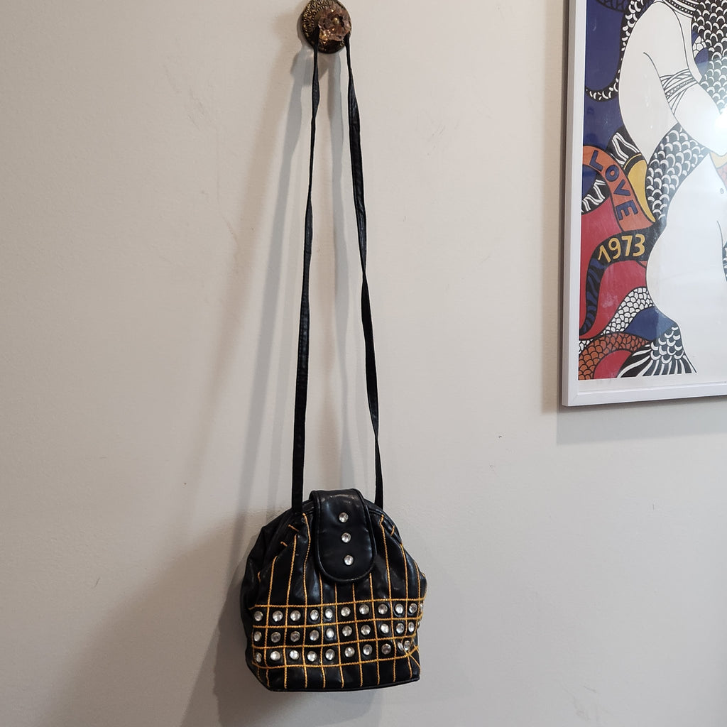 Original photo: black embellished bucket shoulder bag hanging from a wall hook, full-length view of the long shoulder strap