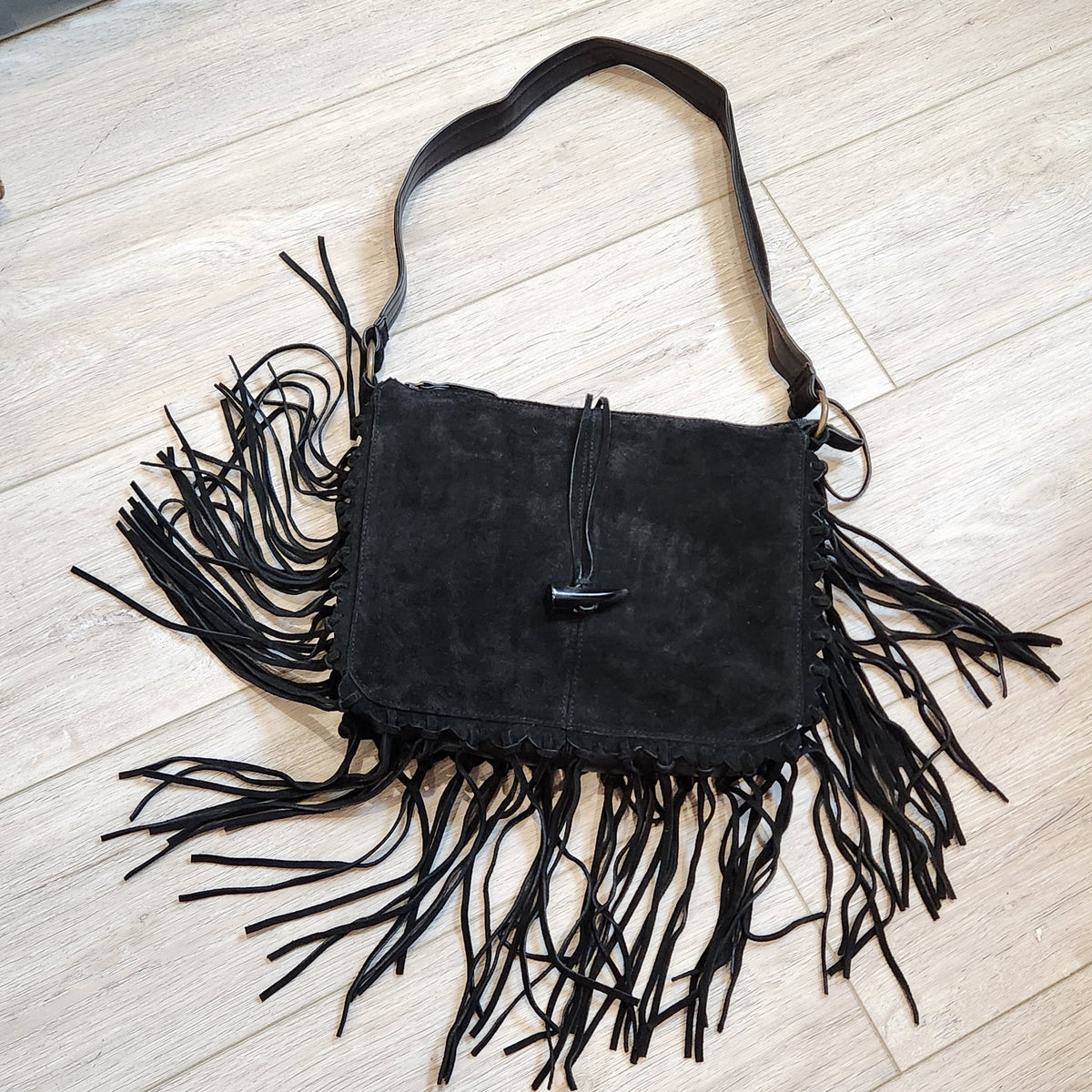 Original photo: vintage EGO black suede fringe shoulder bag, front view on a light wood floor, alternate angle