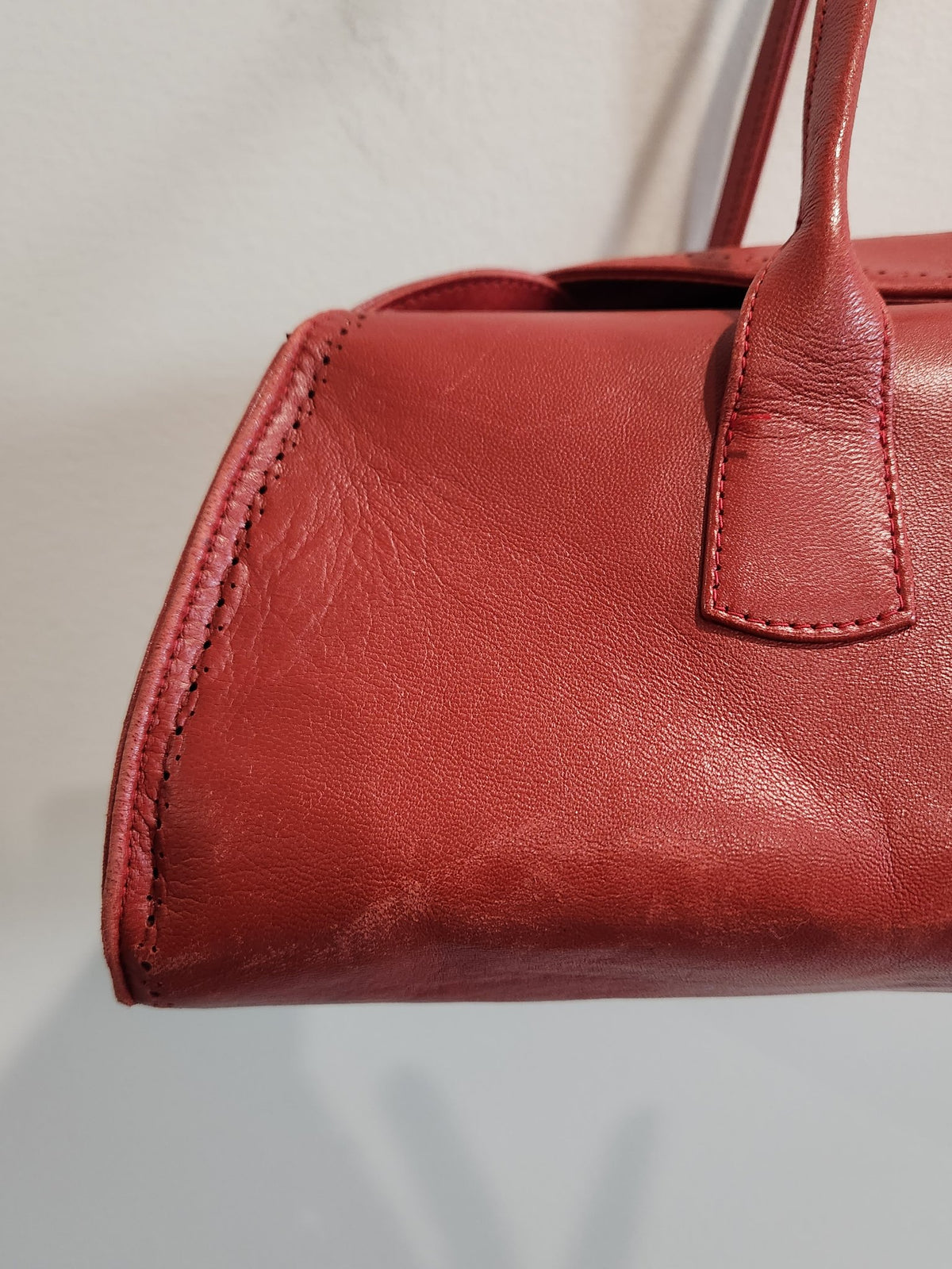 Close-up end detail of vintage Robinson Valentine brick-red leather barrel shoulder bag, showing perforated stitching