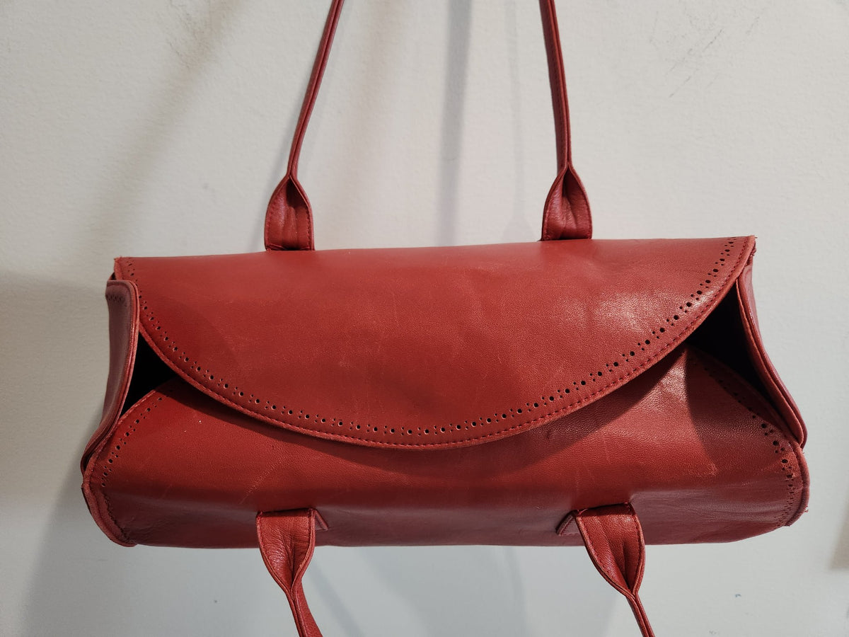 Close-up of the overlapping front flap of vintage Robinson Valentine brick-red leather barrel shoulder bag with perforated detailing