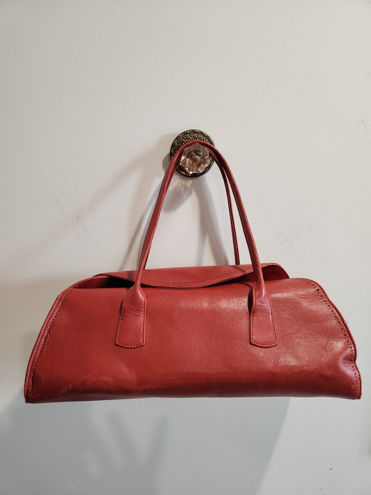 Front view of vintage Robinson Valentine brick-red leather barrel shoulder bag hanging, showing shoulder straps