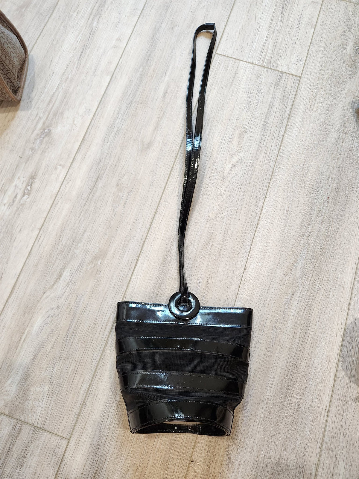 Long slender black patent shoulder strap of vintage Linda Allard for Ellen Tracy bucket bag laid out, showing circular ring attachment