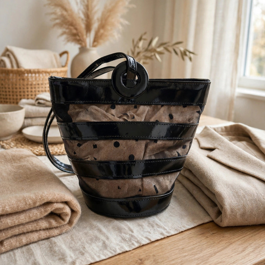 Editorial style shot of vintage Linda Allard for Ellen Tracy black patent leather and sheer mesh bucket bag in a warm neutral interior with folded cashmere