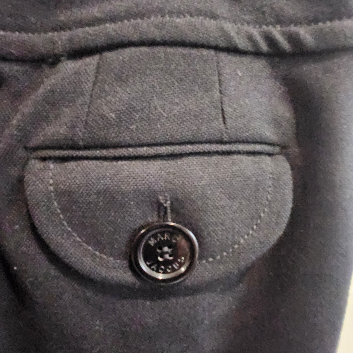 Close-up of a black wool trouser pocket with a button flap featuring the Lucille Golden Vintage, LLC Marc Jacobs logo