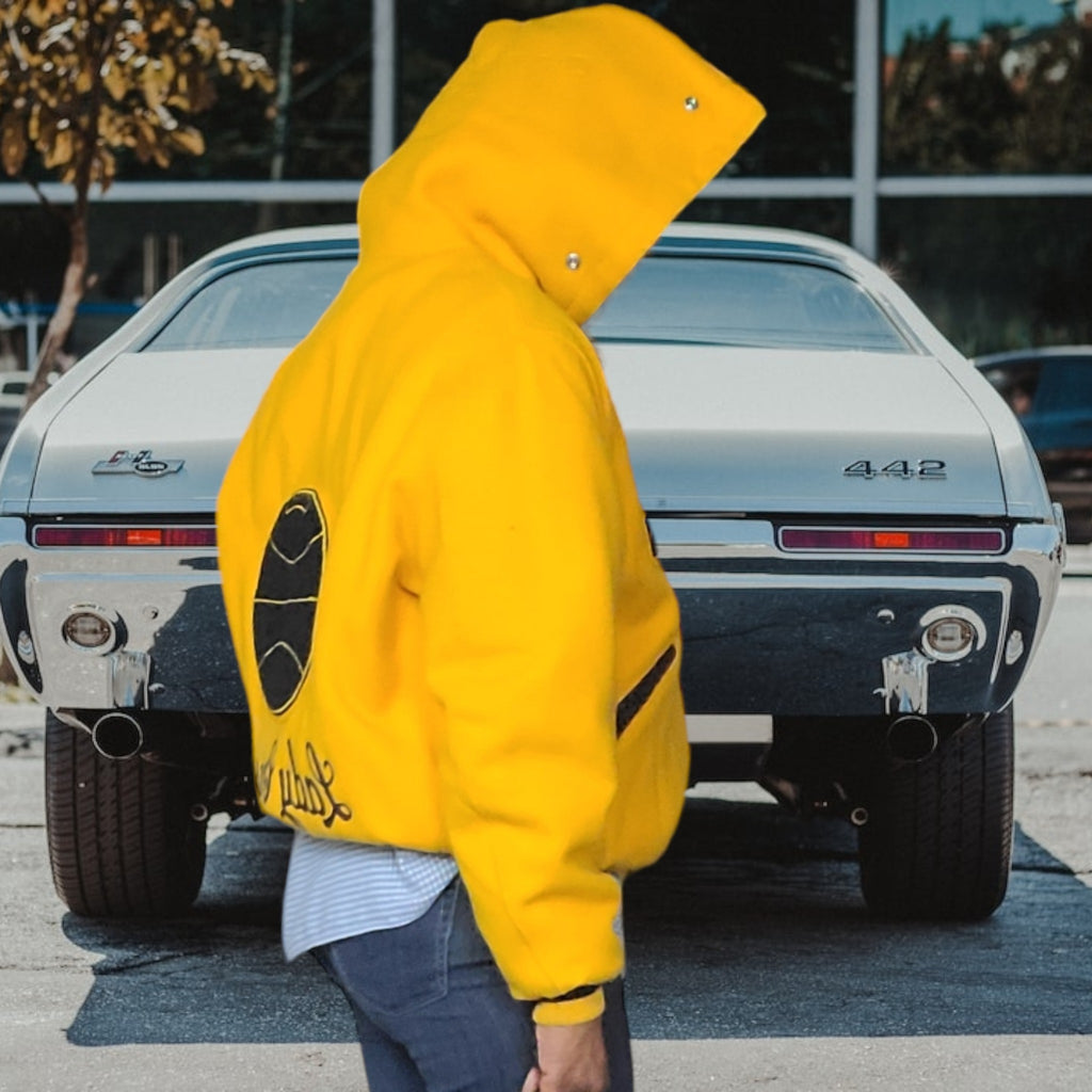Lucille Golden Vintage, LLC 1990s DeLong varsity jacket in gold wool with a unique hood, worn by a person outdoors.