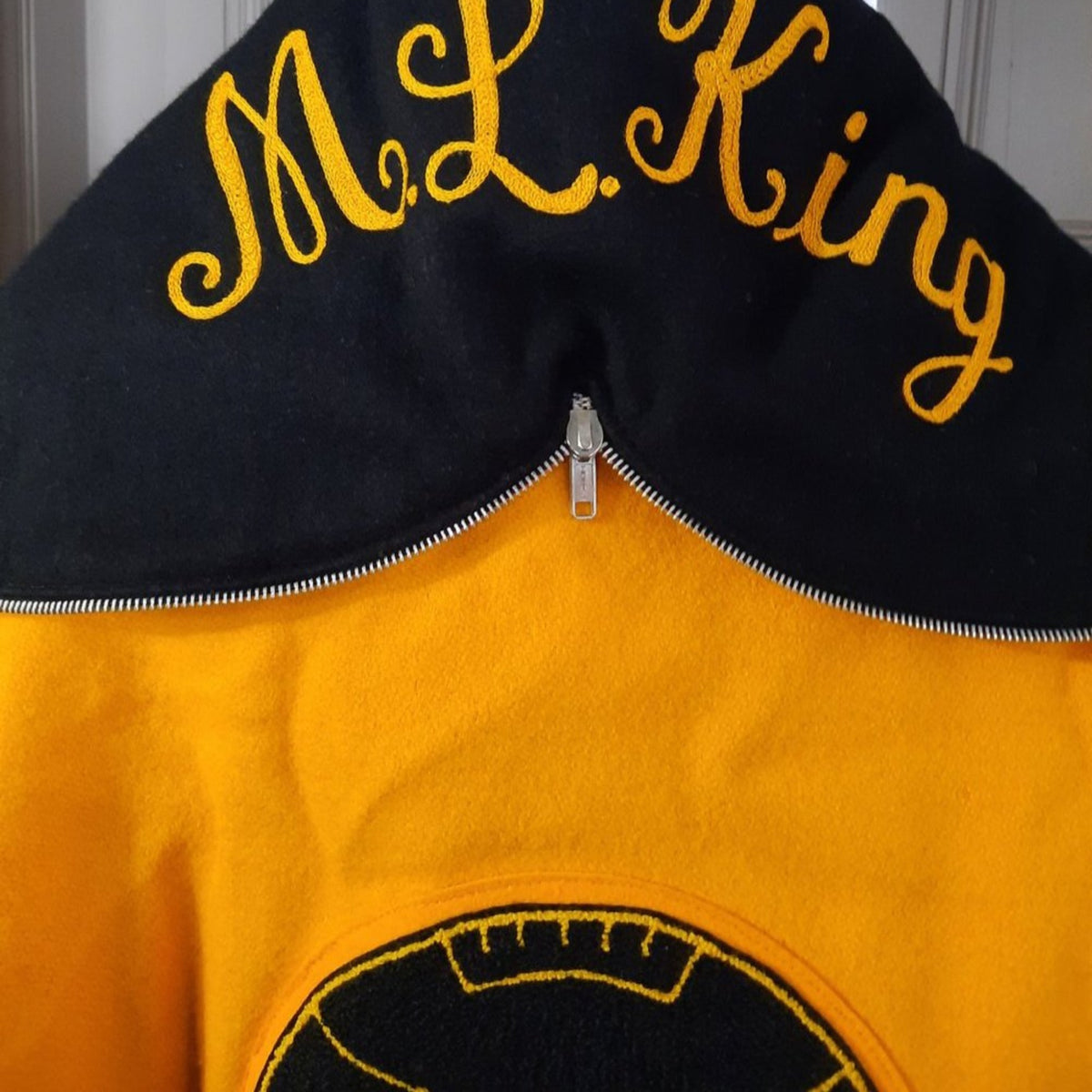 Lucille Golden Vintage, LLC 1990s DeLong varsity jacket with black hood featuring M.L. King embroidery in gold thread.