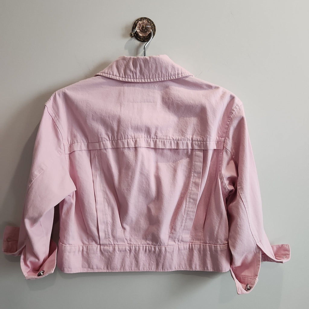 Back view of a Lucille Golden Vintage, LLC pastel pink cropped denim jacket with structured seams hanging on a wall.