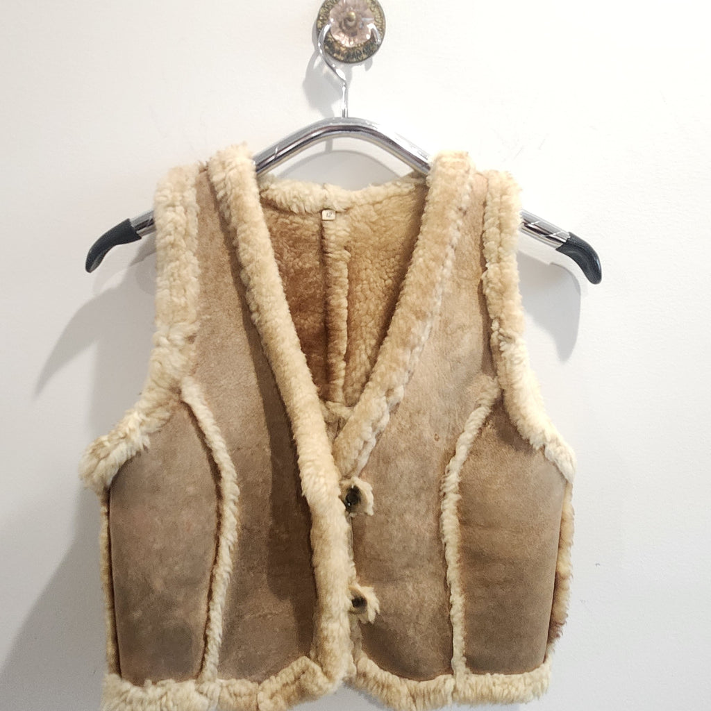 Lucille Golden Vintage, LLC tan suede vest with cream shearling lining and button-front closure on a hanger.
