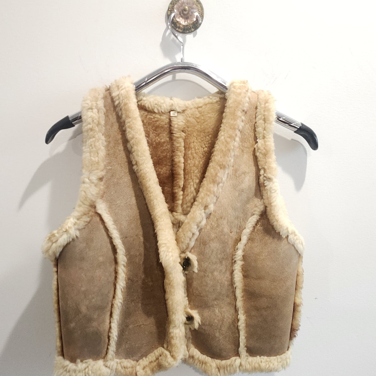 Lucille Golden Vintage, LLC tan suede vest with cream shearling lining and button-front closure on a hanger.