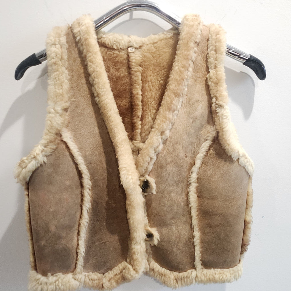 Lucille Golden Vintage, LLC tan suede shearling vest with cream wool trim and button-front closure on a hanger