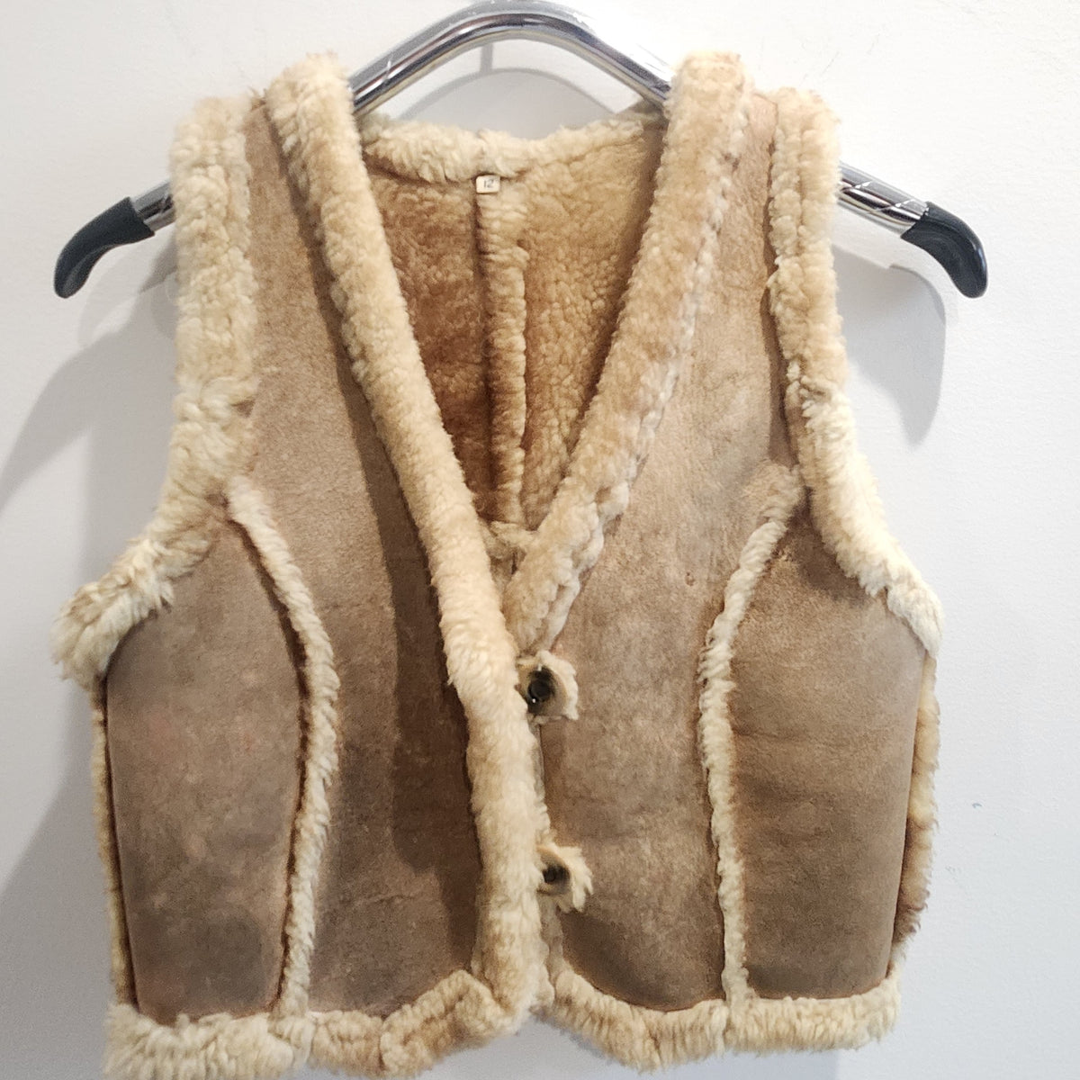 Lucille Golden Vintage, LLC tan suede shearling vest with cream wool trim and button-front closure on a hanger