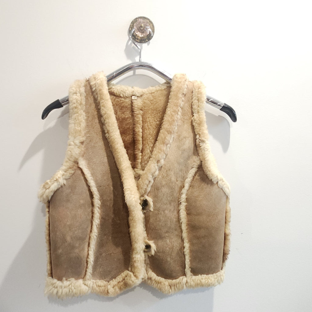Lucille Golden Vintage, LLC tan suede vest with plush cream shearling lining and button-front closure on a hanger.