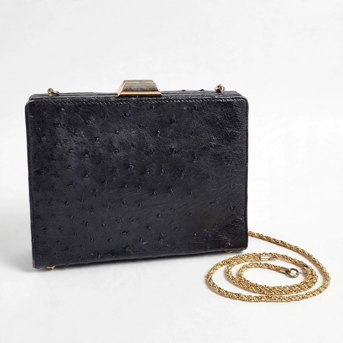 Front view of vintage Beoni Lucia black ostrich-textured leather evening bag on a white background, with braided gold-tone chain strap arranged beside it