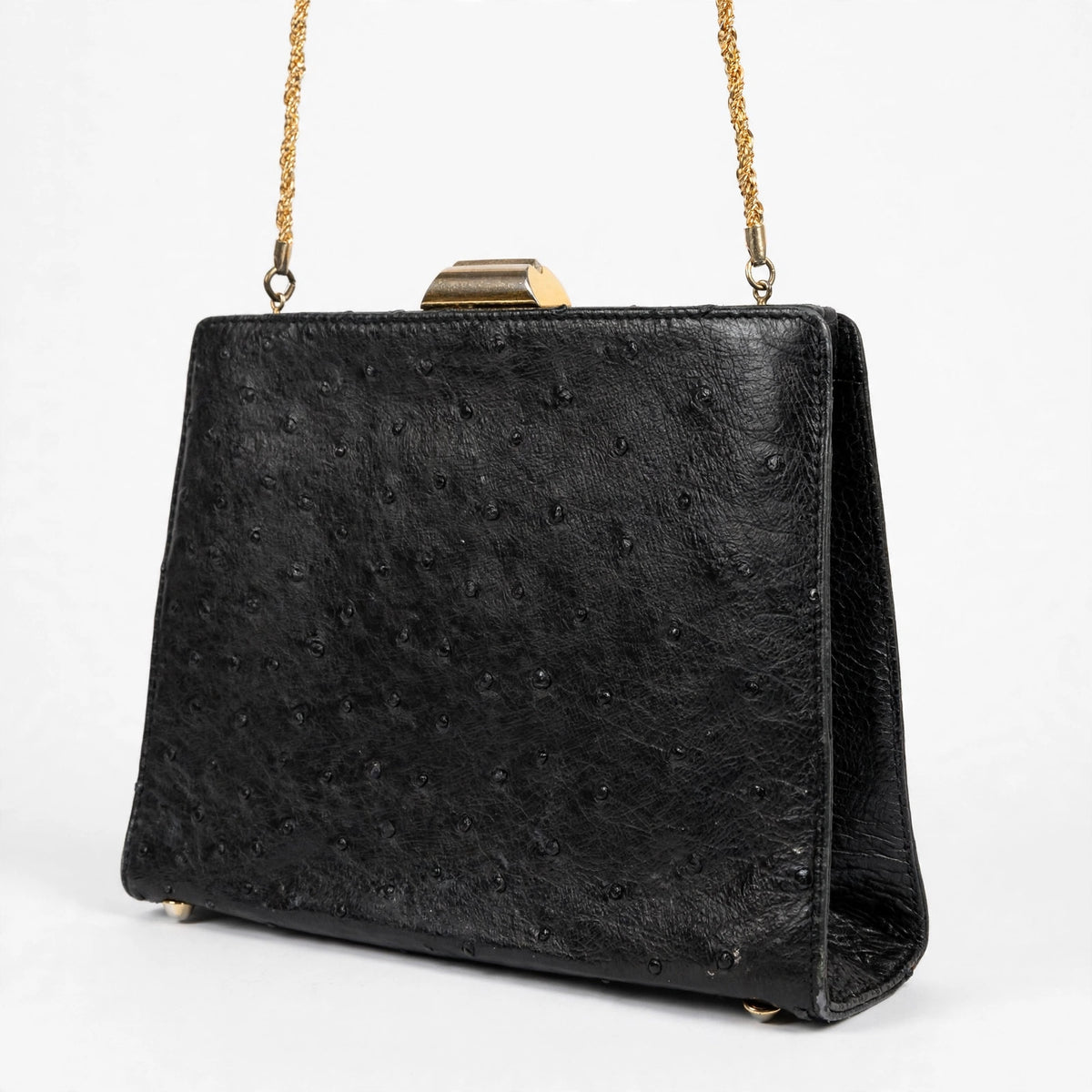Angled front view of vintage Beoni Lucia black ostrich-textured leather evening bag on a white background, showing structured shape and gold-tone geometric clasp