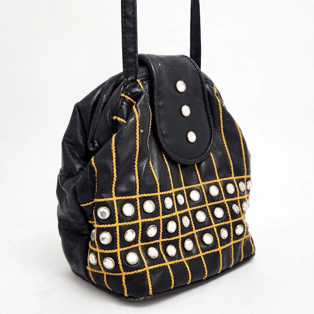 Black embellished bucket shoulder bag on a white background, angled front view showing gold grid embroidery and crystal-style studs