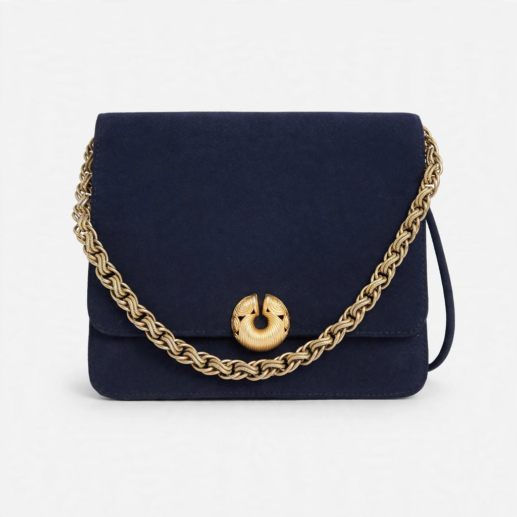 Vintage Kenneth Jay Lane midnight navy flap bag on a white background, front view with gold chain draped across the front and sculptural gold clasp